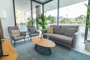 Un salon moderne avec un canapé gris, deux fauteuils, une table basse en bois et une grande fenêtre donnant sur la ville.