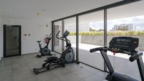 A modern gym with two stationary bikes and a treadmill, large windows offering a view of the city. - Lagos Deluxe 2 With Pool by Homing (Lagos)