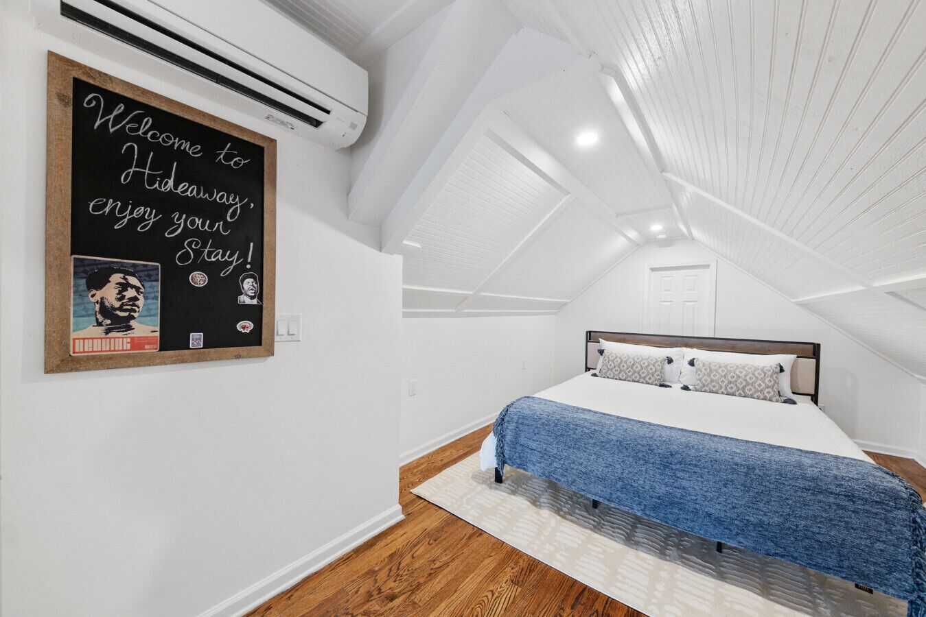 A bedroom with a bed, a wall-mounted air conditioner, and a welcome sign.