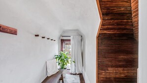 A narrow hallway with a wooden bench, a potted plant, and a sign that reads "WATCH YOUR STEP".