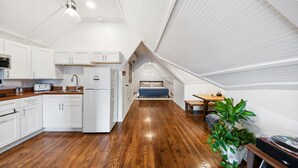 A modern loft bedroom with a sloped ceiling, a kitchenette, and a dining area.