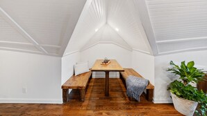 A loft-style room with a wooden dining table and benches, a potted plant, and a white ceiling with exposed beams.