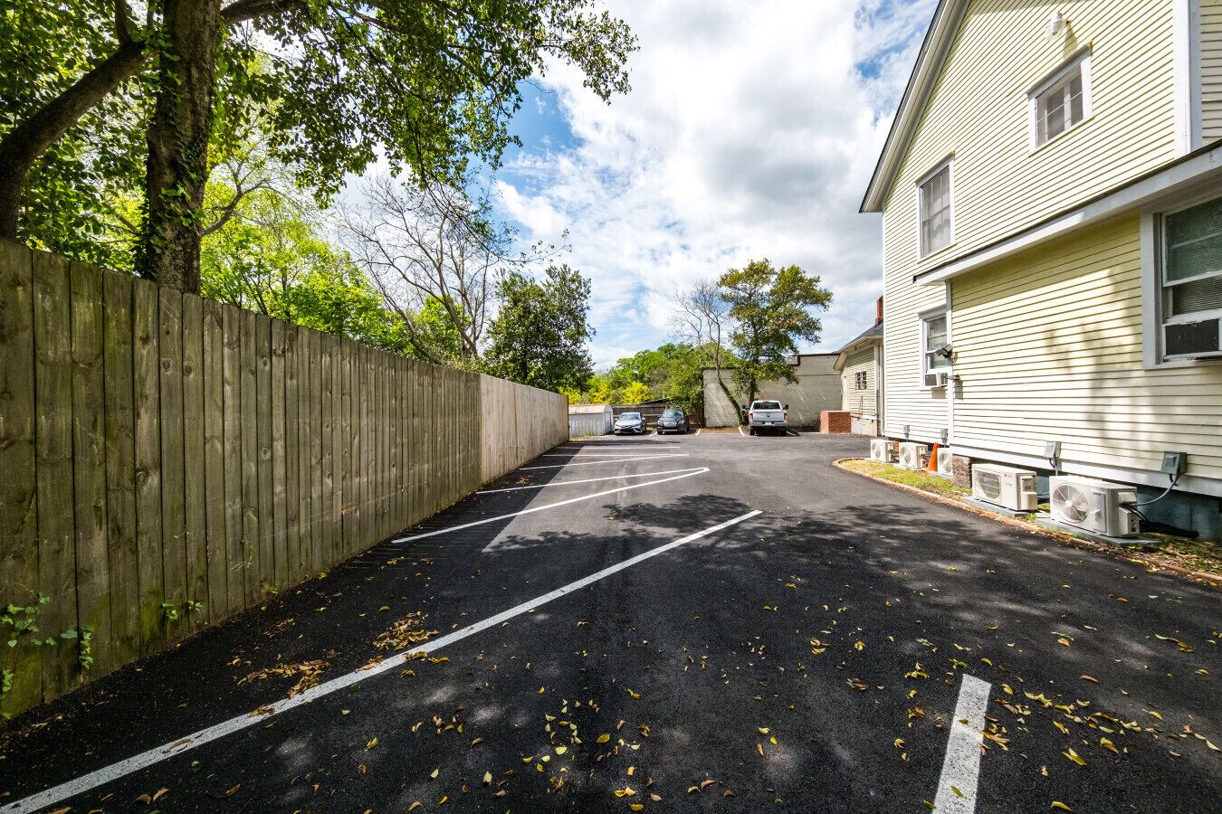 Un parking délimité par une clôture en bois, un bâtiment équipé de climatiseurs et un ciel dégagé.