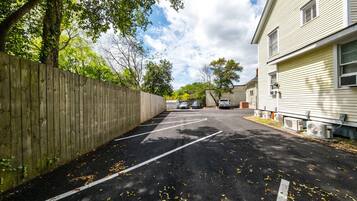 Un parking délimité par une clôture en bois, un bâtiment équipé de climatiseurs et un ciel dégagé.