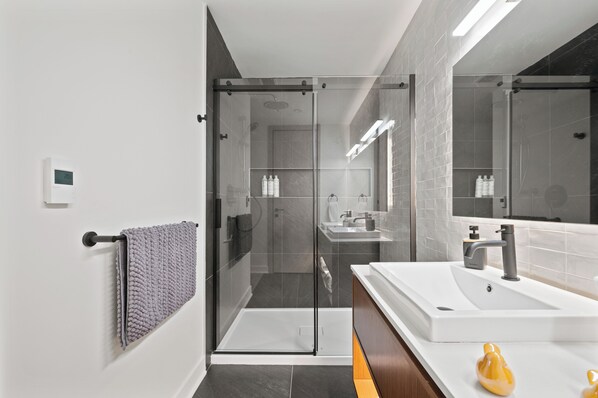A modern bathroom with a glass-enclosed shower, a large white sink, and a mirror.