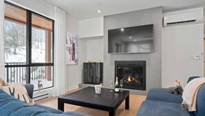 A modern living room with a fireplace, large windows, and a cozy seating area. - Ostrya 203 Ski-in/Ski-Out, Steps from the Slopes! (Mont-Tremblant)