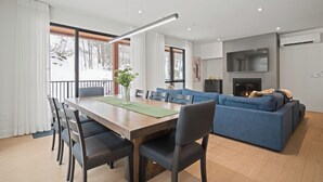 A modern living room with a sofa, a dining table with chairs, and a fireplace. - Ostrya 203 Ski-in/Ski-Out, Steps from the Slopes! (Mont-Tremblant)