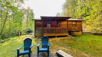 A cabin with a porch, two Adirondack chairs, and a log fire.