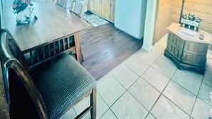 Una cocina funcional con armarios de madera, una mesa de comedor con sillas, un refrigerador y una lámpara sobre una mesita auxiliar.
