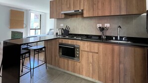 A modern kitchen with wooden cabinets, a built-in oven, a gas stove, and a large island with bar stools. - Modern apartment in La Candelaria - Bogota (Bogotá)