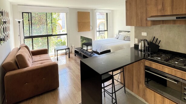 A modern kitchen with a central island, wooden cabinets, and a large window providing natural light. - Modern apartment in La Candelaria - Bogota (Bogotá)