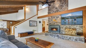 Un salon chaleureux avec une cheminée en pierre, un escalier et un coin repas.