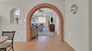 Ein geräumiger Wohnbereich mit einem Ziegelbogen, der in einen Essbereich führt. Es gibt einen Deckenventilator, einen Fernseher und ein Schild mit der Aufschrift 'blessed'.