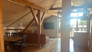 Ein geräumiges Loft mit Holzbalken, einem Essbereich und einem großen Fenster.