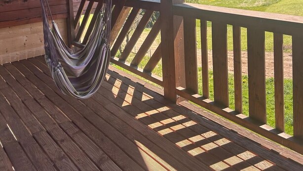 Eine Holzterrasse mit einer Hängematte, Holzgeländern und Blick auf eine grüne Landschaft.