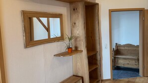 Ein Zimmer mit Holzbalken, einer Holzbank, einem Regal mit Topfpflanze und einem Fenster.