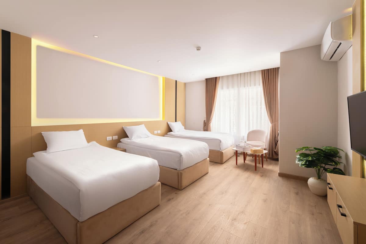 Habitación de hotel con tres camas individuales, una mesita, una silla y un televisor.