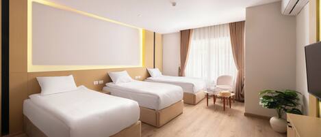 A hotel room with three single beds, a small table, a chair, and a TV.