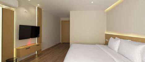 A modern hotel room with a large bed, a flat-screen TV mounted on a wooden console, and a small trash bin.