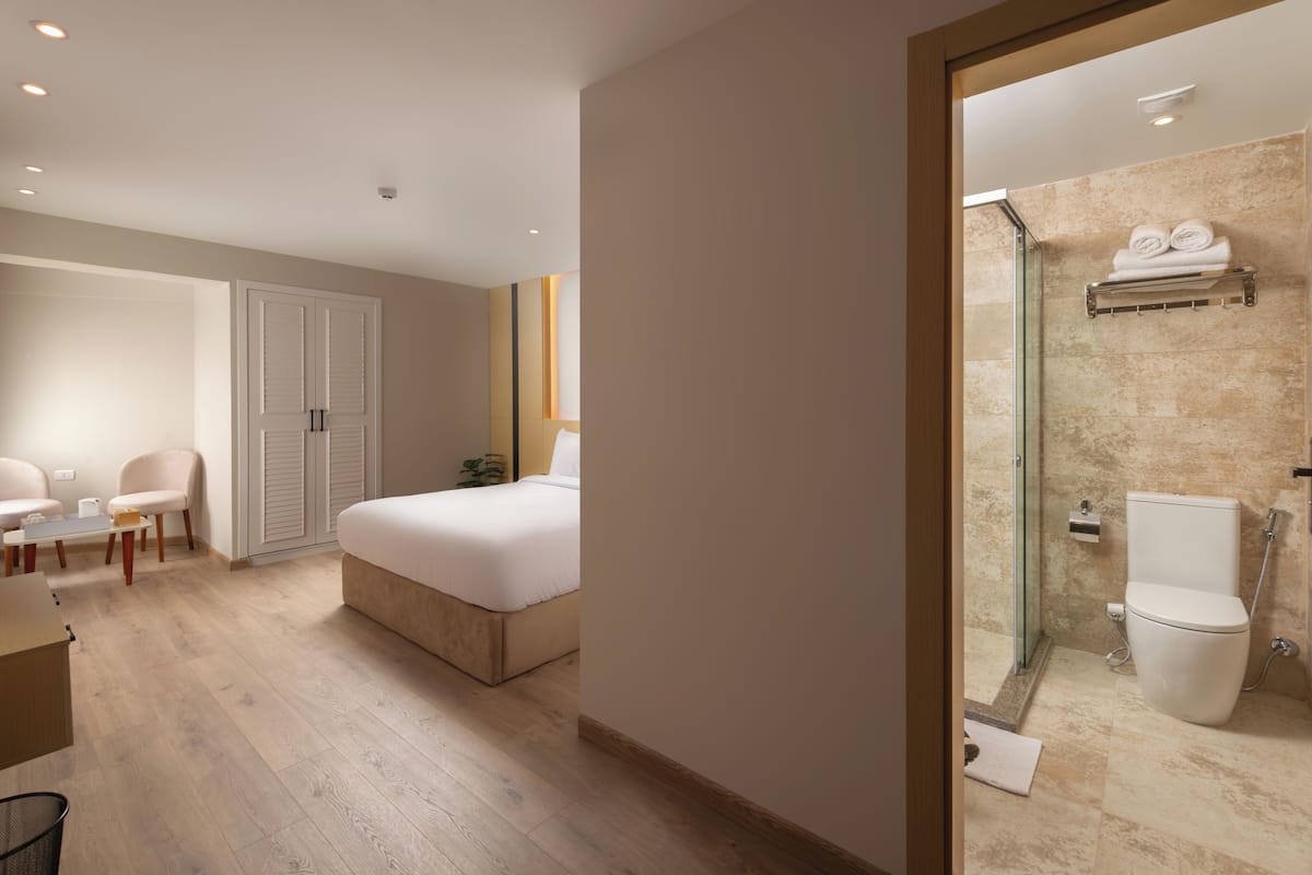 Una habitación de hotel con cama, escritorio, silla, armario y baño con ducha e inodoro.