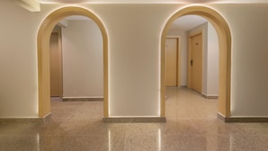 Een hal met twee boogvormige doorgangen naar kamers, een gepolijste tegelvloer en een plafond met inbouwverlichting.