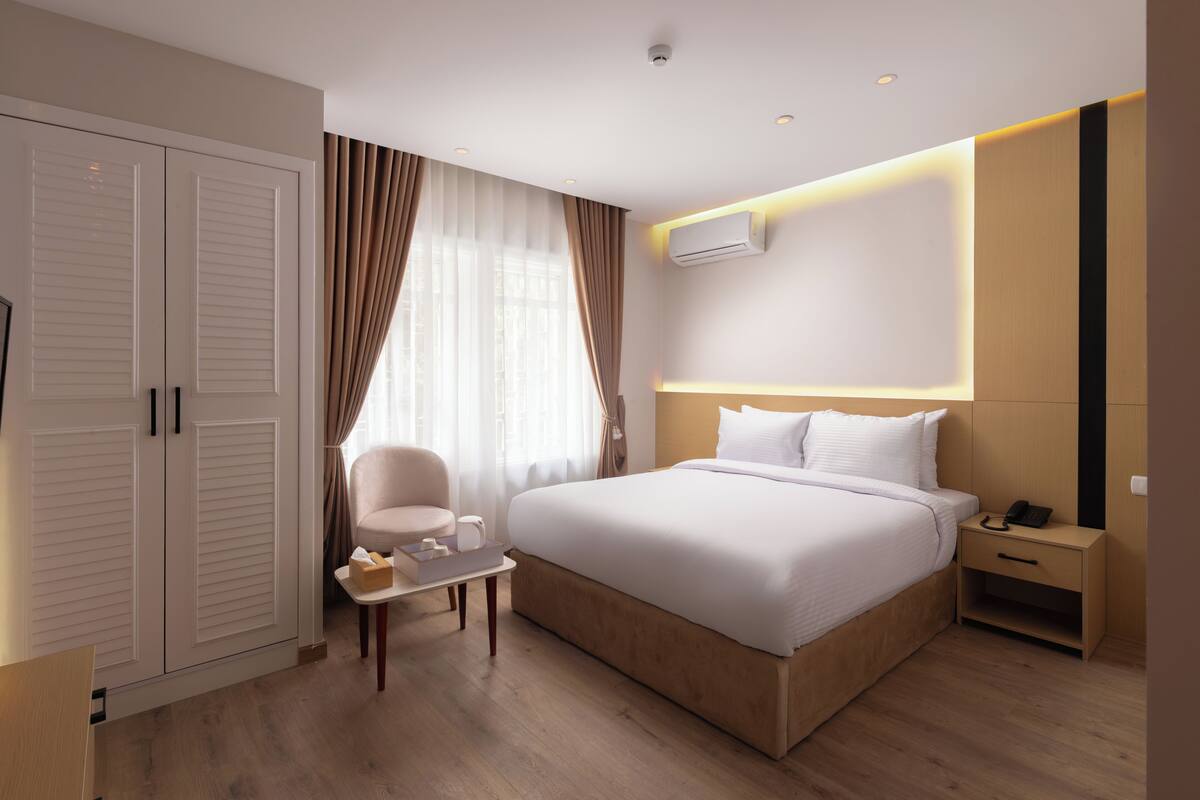 Una habitación de hotel con una cama grande, una mesita de noche con lámpara, una silla y un armario.