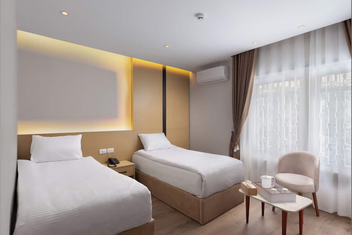 Habitación de hotel con dos camas, una mesita con una silla, una mesita de noche con un teléfono y un equipo de aire acondicionado en la pared.
