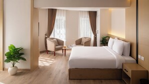 Een hotelkamer met een groot bed, twee fauteuils, een bijzettafeltje en een potplant.