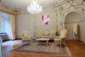 A room with ornate furniture, a chandelier, and a large window with curtains.