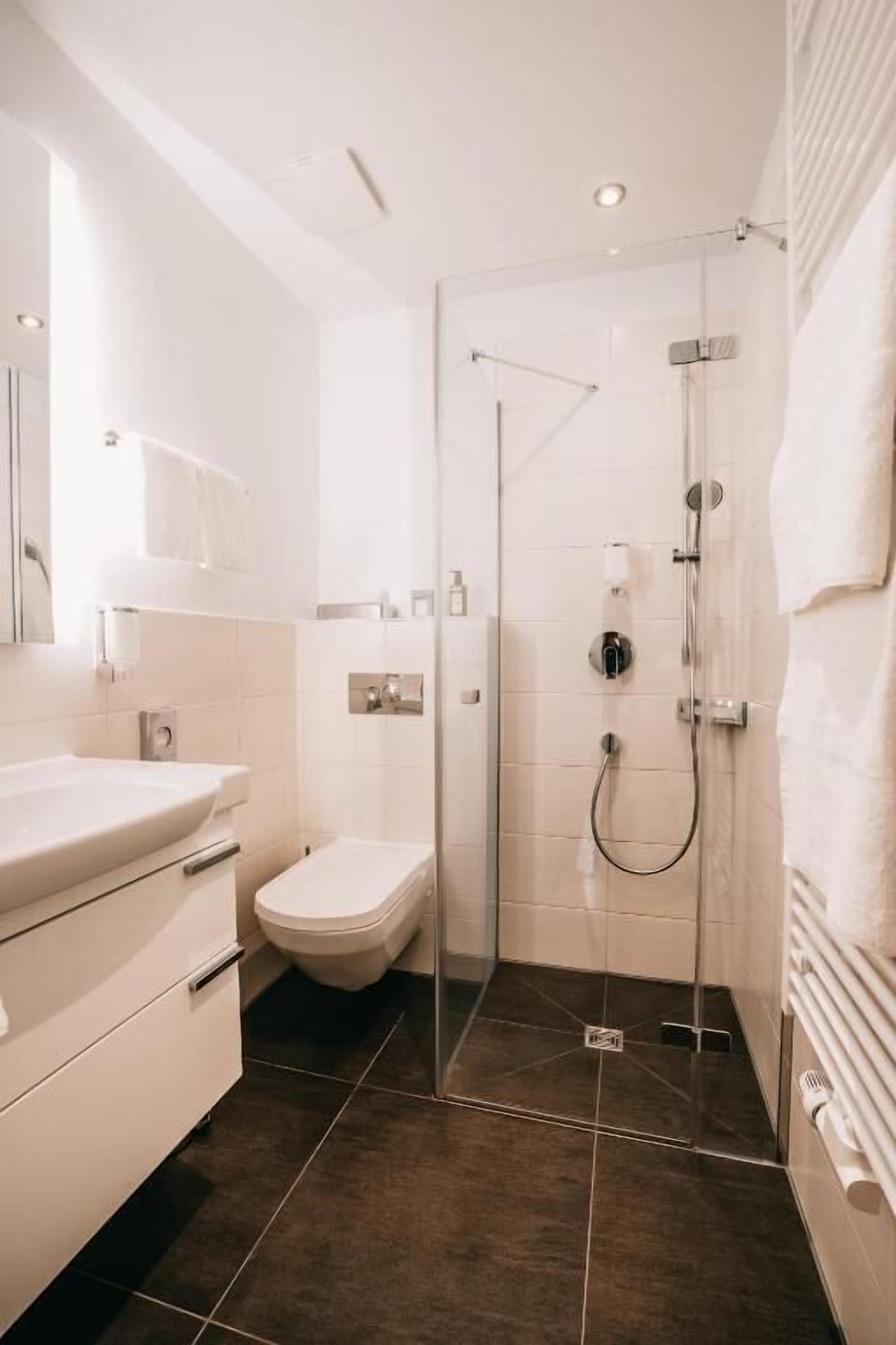 A modern bathroom with a glass shower enclosure, a white sink, and a toilet.