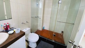 A bathroom with a glass-enclosed shower, a white toilet, and a sink with toiletries. - Refined 3BR Duplex with Ocean Charm (Lima)