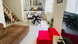 A living room with a brown sofa, a red table, and a TV stand. There is a staircase leading to another room. - Refined 3BR Duplex with Ocean Charm (Lima)
