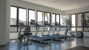 A gym with treadmills and exercise bikes, large windows, and a view of palm trees. - I Soho at I City by My Trip & My Stay (Shah Alam)