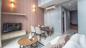 A modern living room with a brick accent wall, a flat-screen TV, a dining area with chairs and a table, and a sofa with a throw pillow. - I Soho at I City by My Trip & My Stay (Shah Alam)