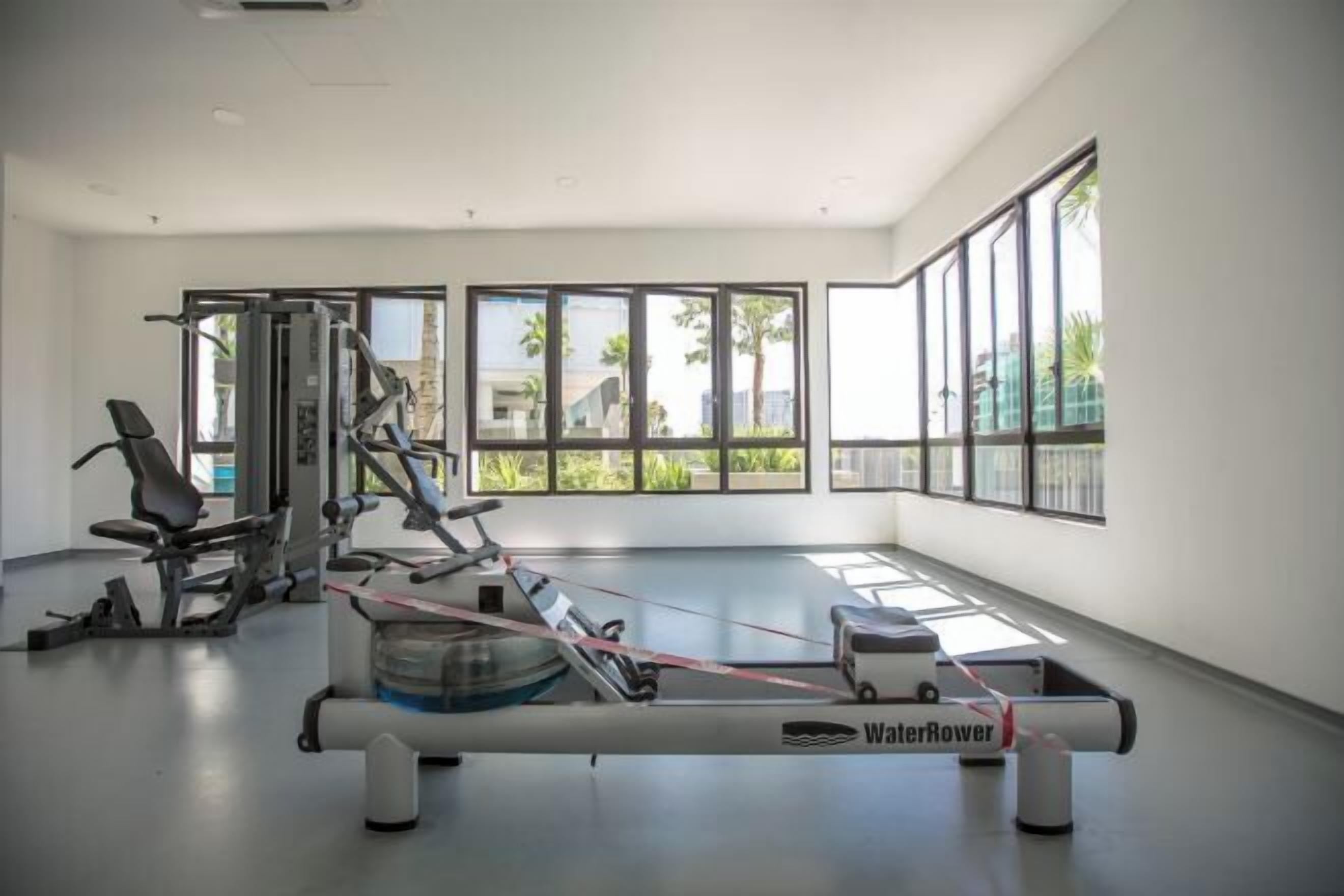A gym with exercise equipment, large windows, and a view of palm trees.