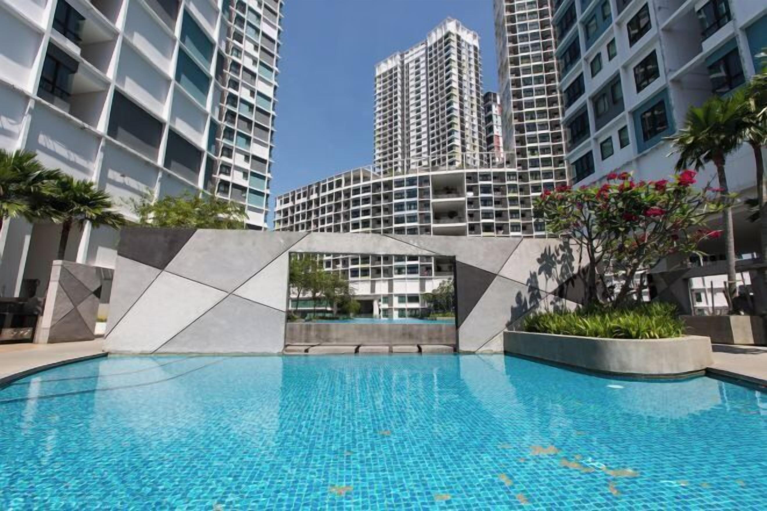 A swimming pool surrounded by high-rise buildings, with a geometric structure in the foreground.