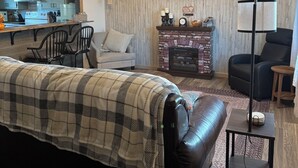 Een moderne woonkamer met een groot bed, een open haard, een televisie en een keuken die in een spiegel zichtbaar is.