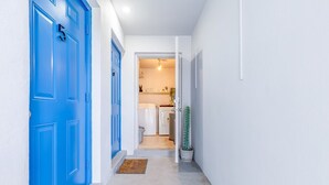 Un couloir avec des portes bleues, un mur blanc et un coin cuisine visible à travers une porte ouverte.