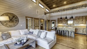 A spacious living area with a large sectional sofa, a wooden coffee table, and a kitchen area with bar stools. - Wanderlust - Mountain views & hot tub (Blue Ridge Mountains)