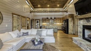 A spacious living room with a large sectional sofa, a fireplace, and a kitchen in the background. - Wanderlust - Mountain views & hot tub (Blue Ridge Mountains)