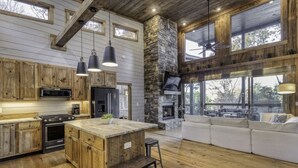 A spacious kitchen with wooden cabinets, a large island, and a stone fireplace. - Wanderlust - Mountain views & hot tub (Blue Ridge Mountains)