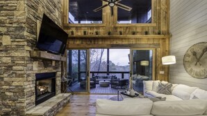 A spacious living area with a stone fireplace, a flat-screen TV, and a large clock on the wall. - Wanderlust - Mountain views & hot tub (Blue Ridge Mountains)