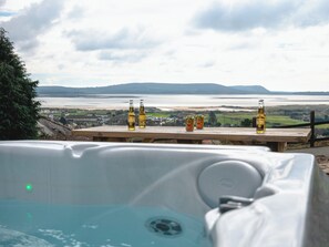 Ein Holztisch mit Corona Extra- und Liptun-Bierflaschen, mit Blick auf ein Gewässer und hügelige Landschaft.