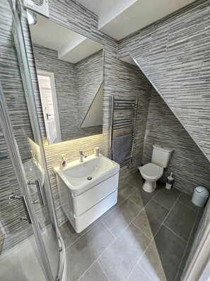 Ein modernes Badezimmer mit Duschkabine aus Glas, einem weißen Waschtisch mit Waschbecken, einer Toilette und einem Handtuchhalter.