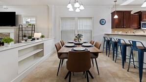 Une cuisine moderne avec un coin repas, comprenant un grand îlot central, des tabourets de bar et un lustre.