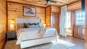 A cozy wooden cabin bedroom with a large bed, two bedside tables, a ceiling fan, and a framed picture on the wall.