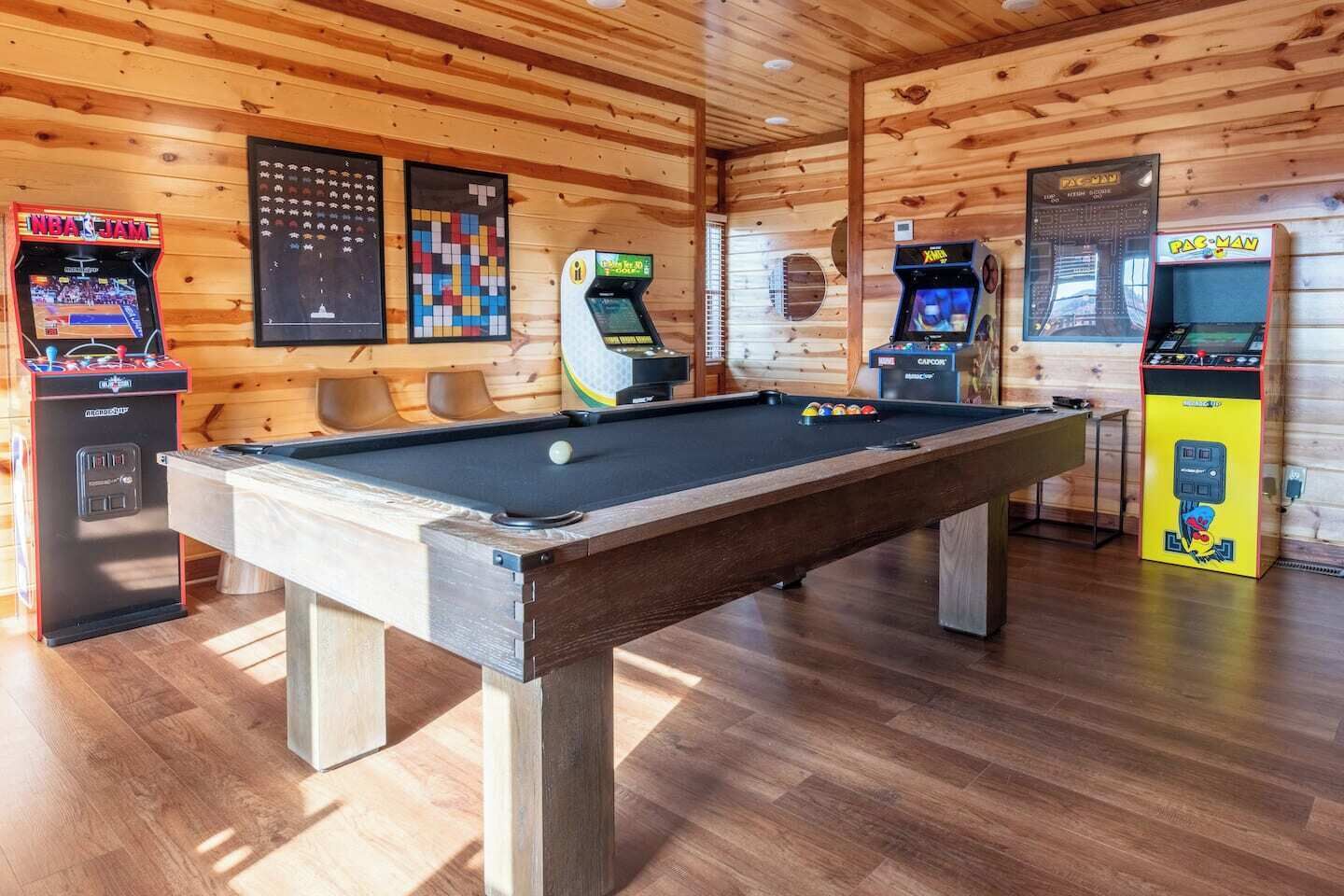 A pool table with four arcade machines, a wooden ceiling, and a billiards table.