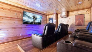 A wooden-paneled room with leather reclining chairs and a large flat-screen TV mounted on the wall.