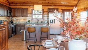 A wooden cabin kitchen with a central island, bar stools, and a dining table set for two.