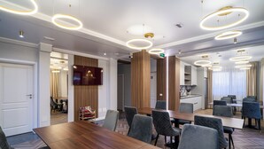 Un salón de conferencias moderno con una larga mesa de madera, múltiples sillas tapizadas en gris y luces de techo circulares.